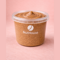 NutHouse almond butter in clear tub showing creamy light brown texture with dark almond specks and swirled peak