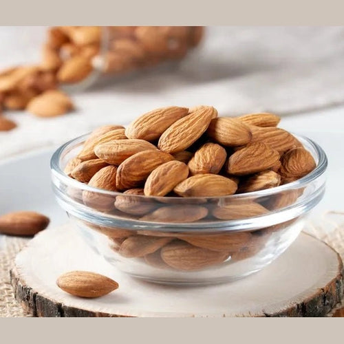 Whole raw almonds in glass bowl on rustic wood slice showing natural texture