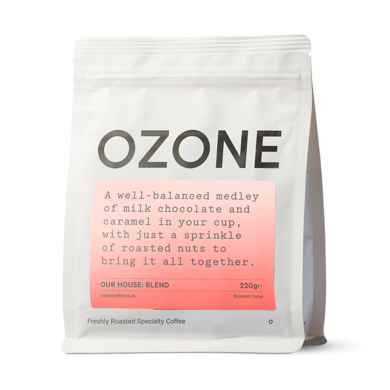Ozone House Blend coffee beans in white matte resealable pouch with salmon-pink label showing milk chocolate and caramel tasting notes
