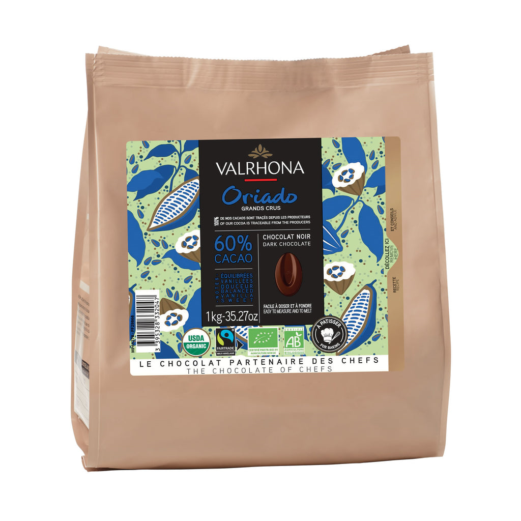 A 1kg bag of Valrhona Orido 60% Cacao dark chocolate, featuring a tan paper bag with a colorful label depicting cocoa plants and a chocolate bean.