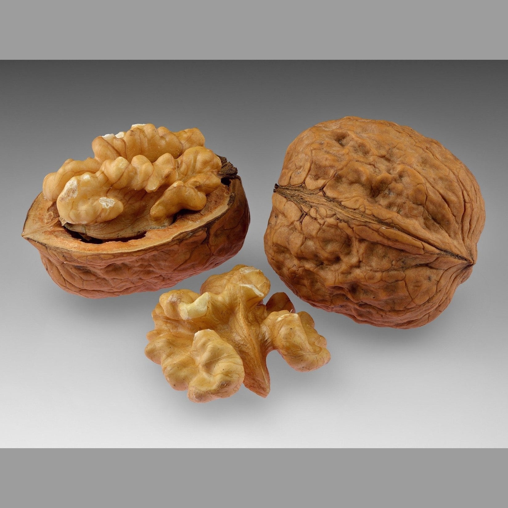 Whole and cracked walnut kernels showing brain-like texture on gray background